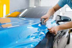 Car wrapping, mechanic with squeegee installs film